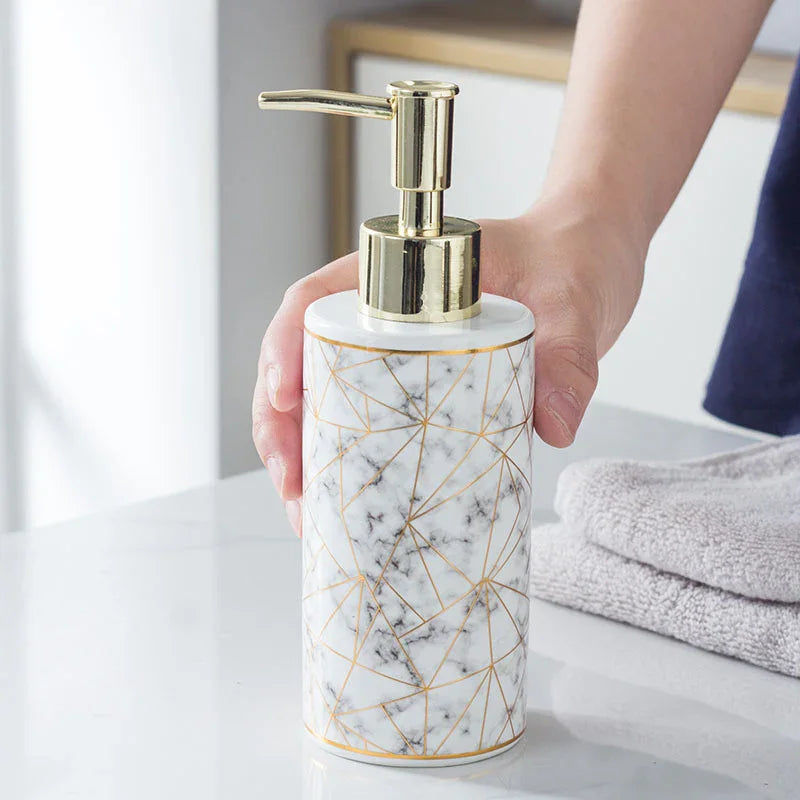 Marble soap dispenser with gold geometric pattern and pump, held in hand on bathroom counter