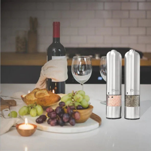 Stainless steel electric salt and pepper grinders on kitchen table with wine, grapes, bread