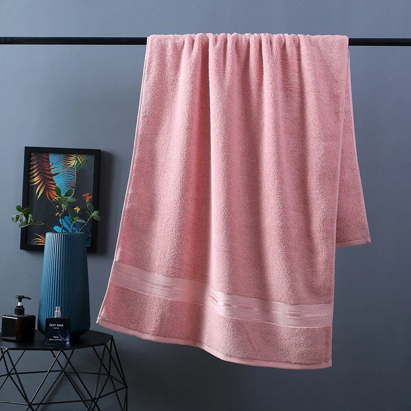 Soft pink bath towel with decorative border, hanging in modern bathroom setting