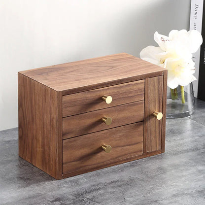 Wooden jewelry box with three drawers and gold knobs on a countertop, flowers in background