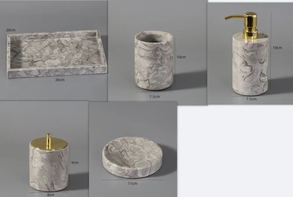 Marble bathroom accessory set with gold accents, including tray, soap dispenser, tumbler, jar, and dish