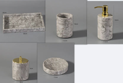 Marble bathroom accessory set with gold accents, including tray, soap dispenser, tumbler, jar, and dish